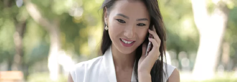 Smiling person talking on a phone outdoors.
