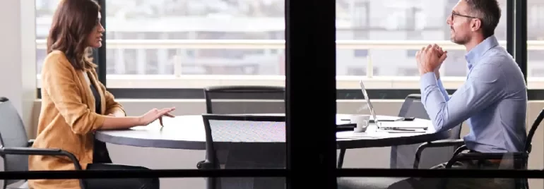 Two people engaged in a discussion at a round table in an office setting.