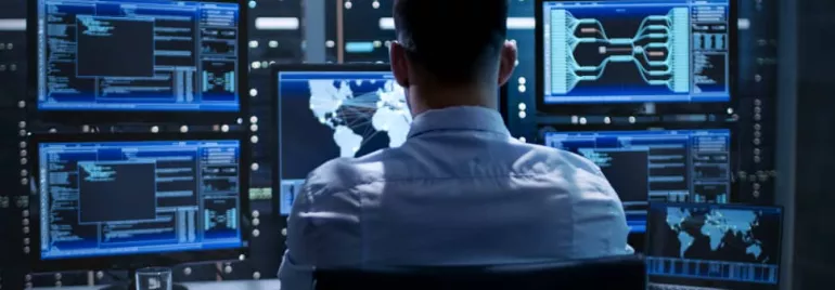 Person working at a desk with multiple computer monitors displaying data and a world map.