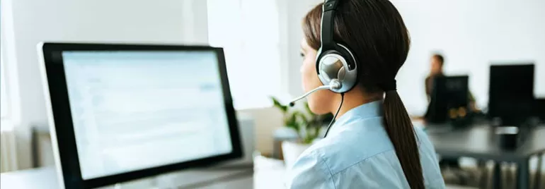 Person at a desk wearing a headset, working on a computer in an office.