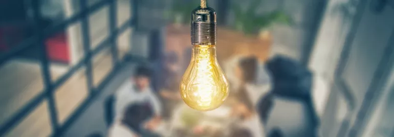 A glowing light bulb above a group of people in a meeting room.