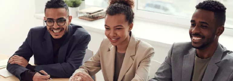 Three people sitting at a table, smiling during a meeting.