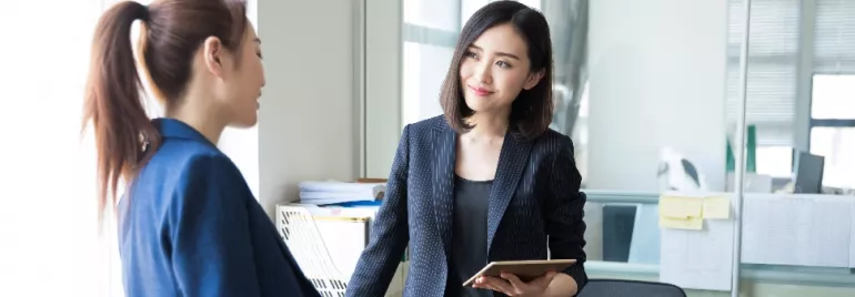 Two people in formal attire having a conversation in an office.