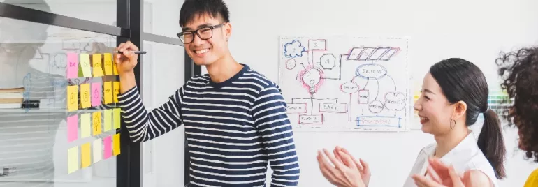 Person smiles while presenting colorful sticky notes on a board.