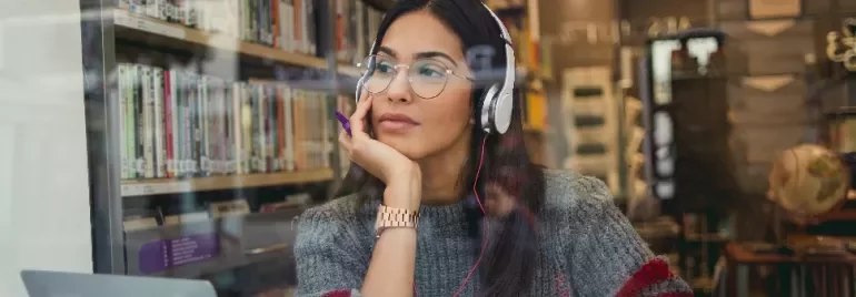 Person wearing headphones sitting in a library, looking thoughtful.