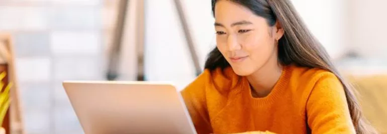Person in orange sweater working on a laptop at home.
