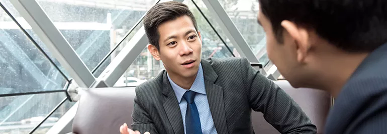 Two people in business attire are engaged in a conversation in an office setting.
