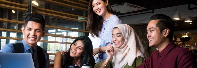 Group of people smiling and discussing around a laptop in a modern office.