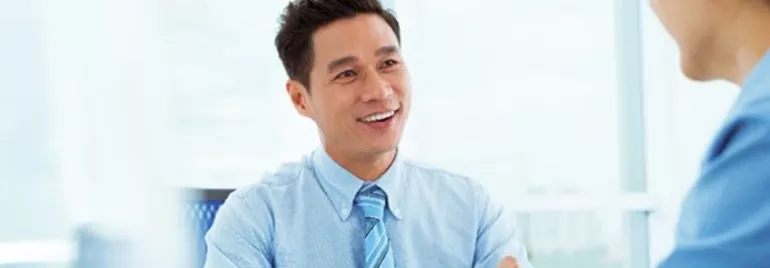 Person in a blue shirt smiling and talking to someone in a light office.