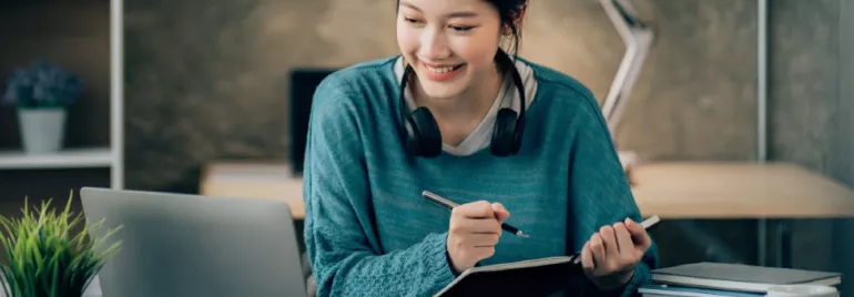 Person with headphones studying on a laptop at a cozy desk.