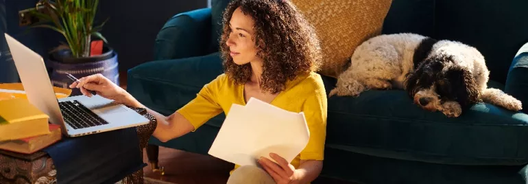Person working at home on a laptop with a dog resting on a sofa.