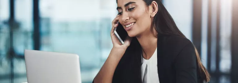 Person smiling while talking on the phone and working on a laptop.