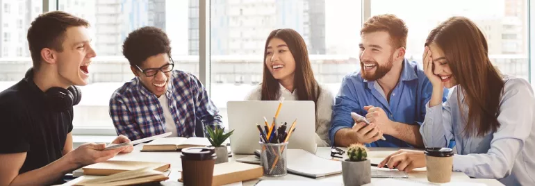 Group of people laughing and studying together at a table.