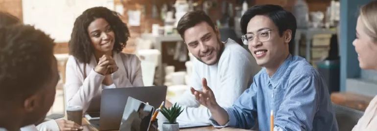Group of people having a meeting around a table with laptops and notebooks.