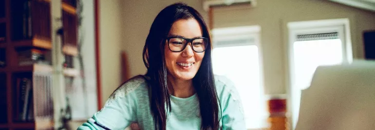 Person smiling while using a laptop at a desk.