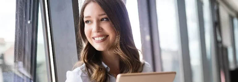 Person smiling while looking out a window with a laptop.