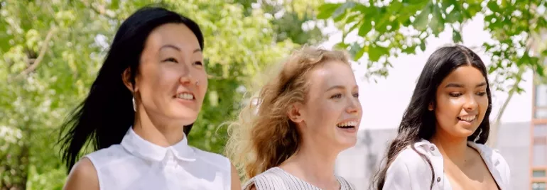 Three people walking outdoors, smiling under the trees.