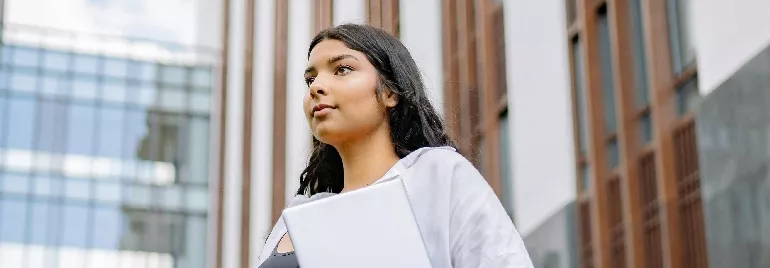 Person holding books, walking near a modern building.