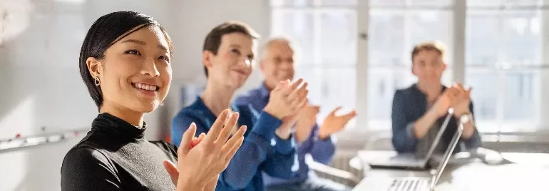 People sitting in a meeting room clapping and smiling.