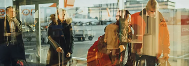Travelers with luggage walk through a bright airport terminal.