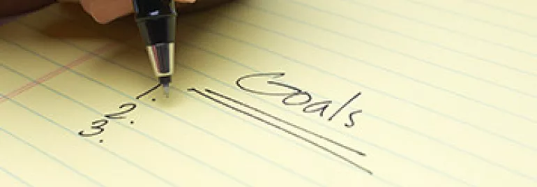 Handwriting goals on a yellow notepad.