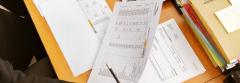 Person holding financial spreadsheets at a desk with a calculator.