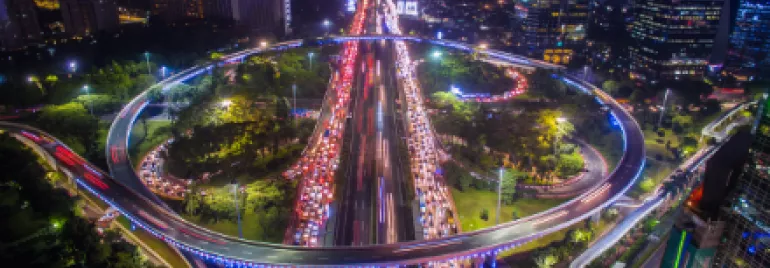 Aerial view of a busy city highway interchange with vibrant lights at night.