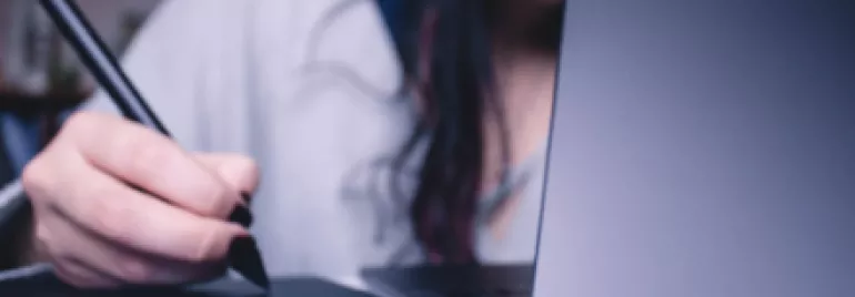 Person using a digital pen and tablet in front of a laptop.