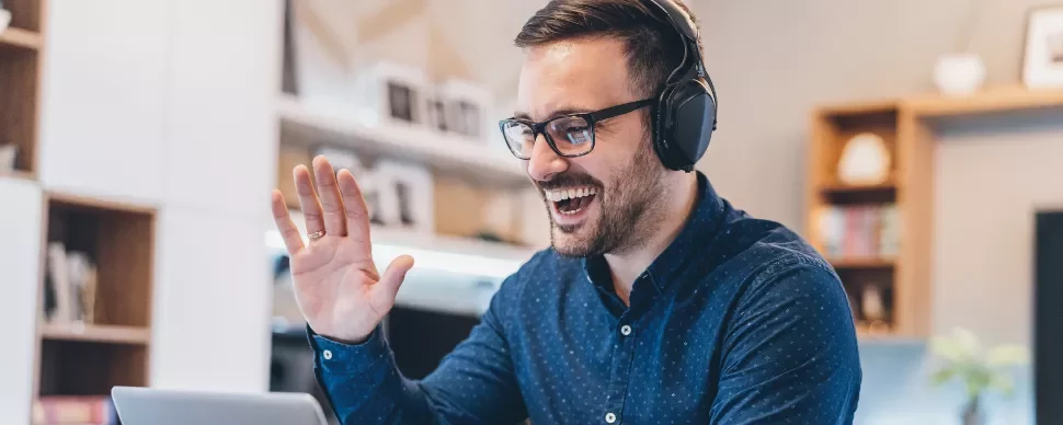 Person wearing headphones, smiling and waving at a laptop.