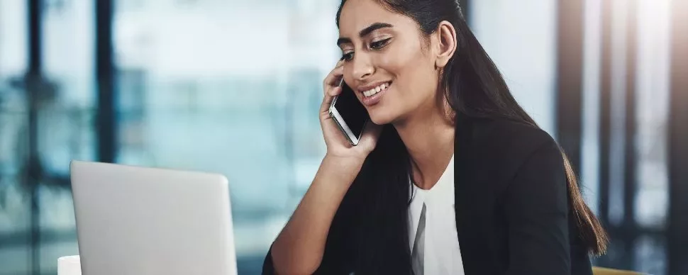Person smiling while talking on the phone and working on a laptop.