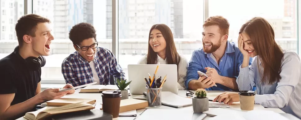 Group of people laughing and studying together at a table.