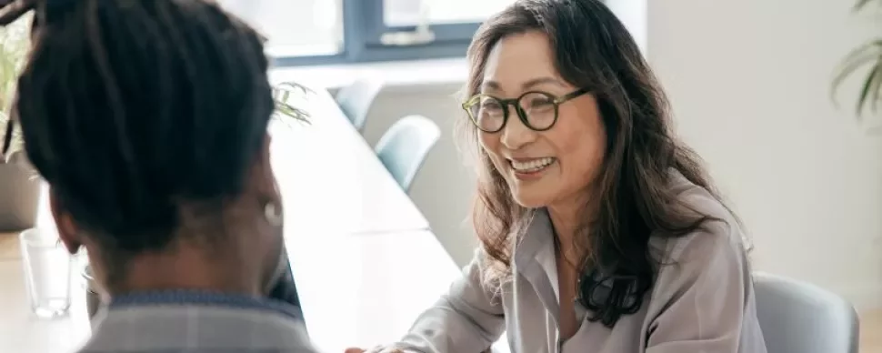 A woman in glasses converses with a man in an office setting, both engaged in discussion.