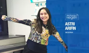 Person smiling with arms outstretched, standing in a lab with shelves and bottles.