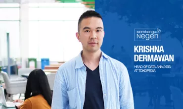 Person standing in an office environment with people working in the background.