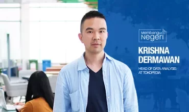 Person standing in an office environment with people working in the background.