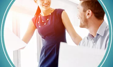 Two people smiling and discussing paperwork at a desk.