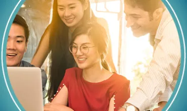 Group of people smiling and looking at a laptop together indoors.