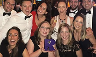 Group of people dressed formally at a celebration, smiling and holding a purple award.