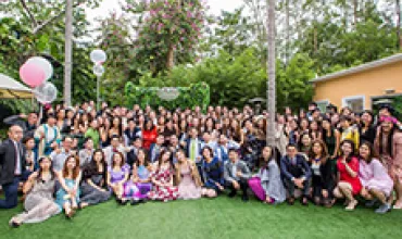Large group gathered in a garden setting with trees and balloons.