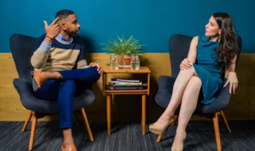 Two people seated in chairs having a conversation in a modern room.