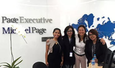 Four people smiling in an office with a world map on the wall.