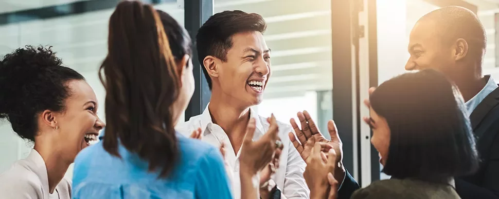 A group of people laughing and clapping in an office setting.