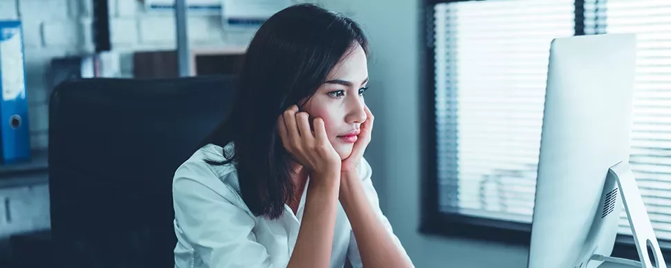 Person sitting at desk, looking at computer screen in bright office.