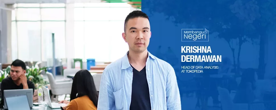 Person standing in an office environment with people working in the background.