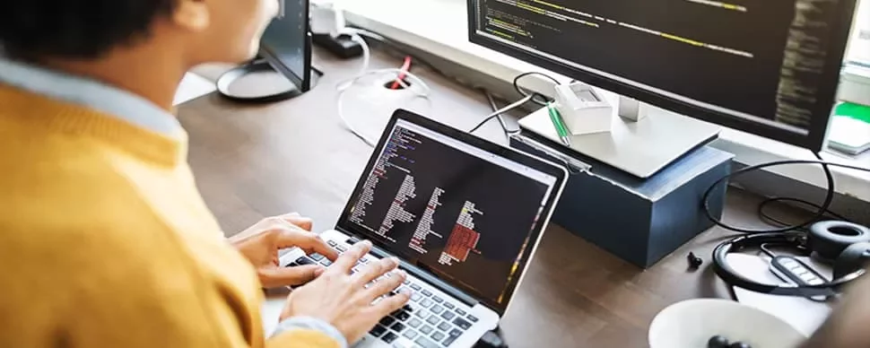 Person coding on a laptop with a monitor displaying code