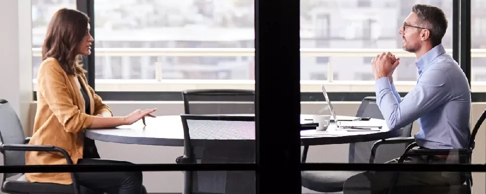 Two people engaged in a discussion at a round table in an office setting.