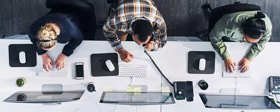 Three people working at computers in a modern office space.