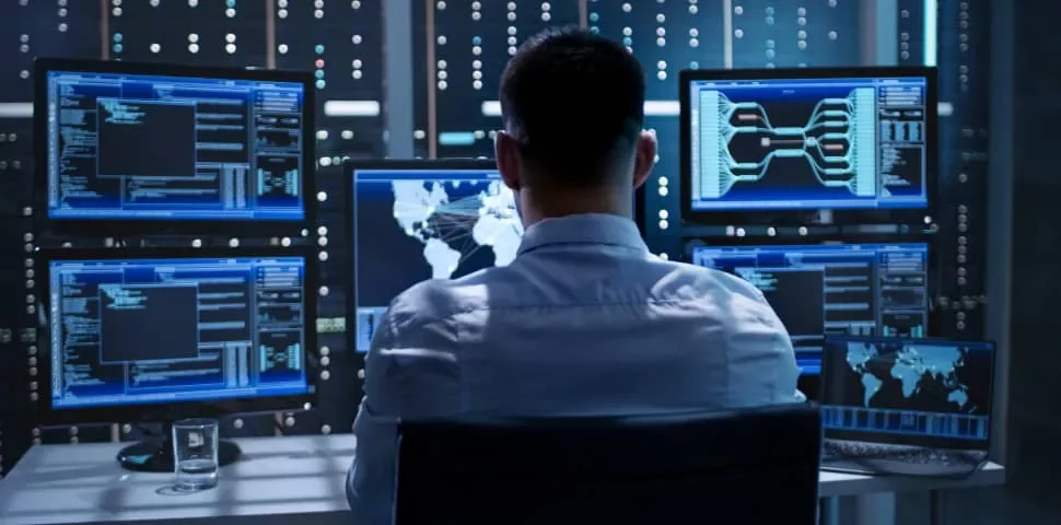 Person working at a desk with multiple computer monitors displaying data and a world map.