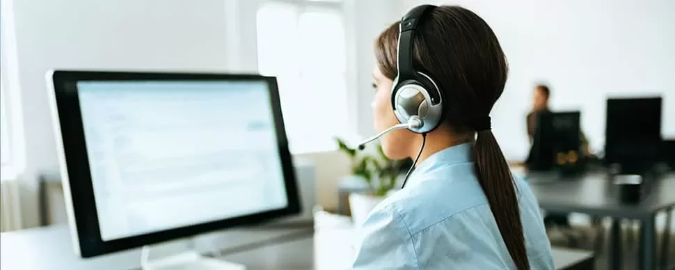 Person at a desk wearing a headset, working on a computer in an office.