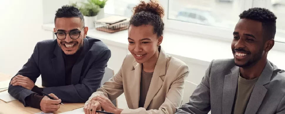 Three people sitting at a table, smiling during a meeting.